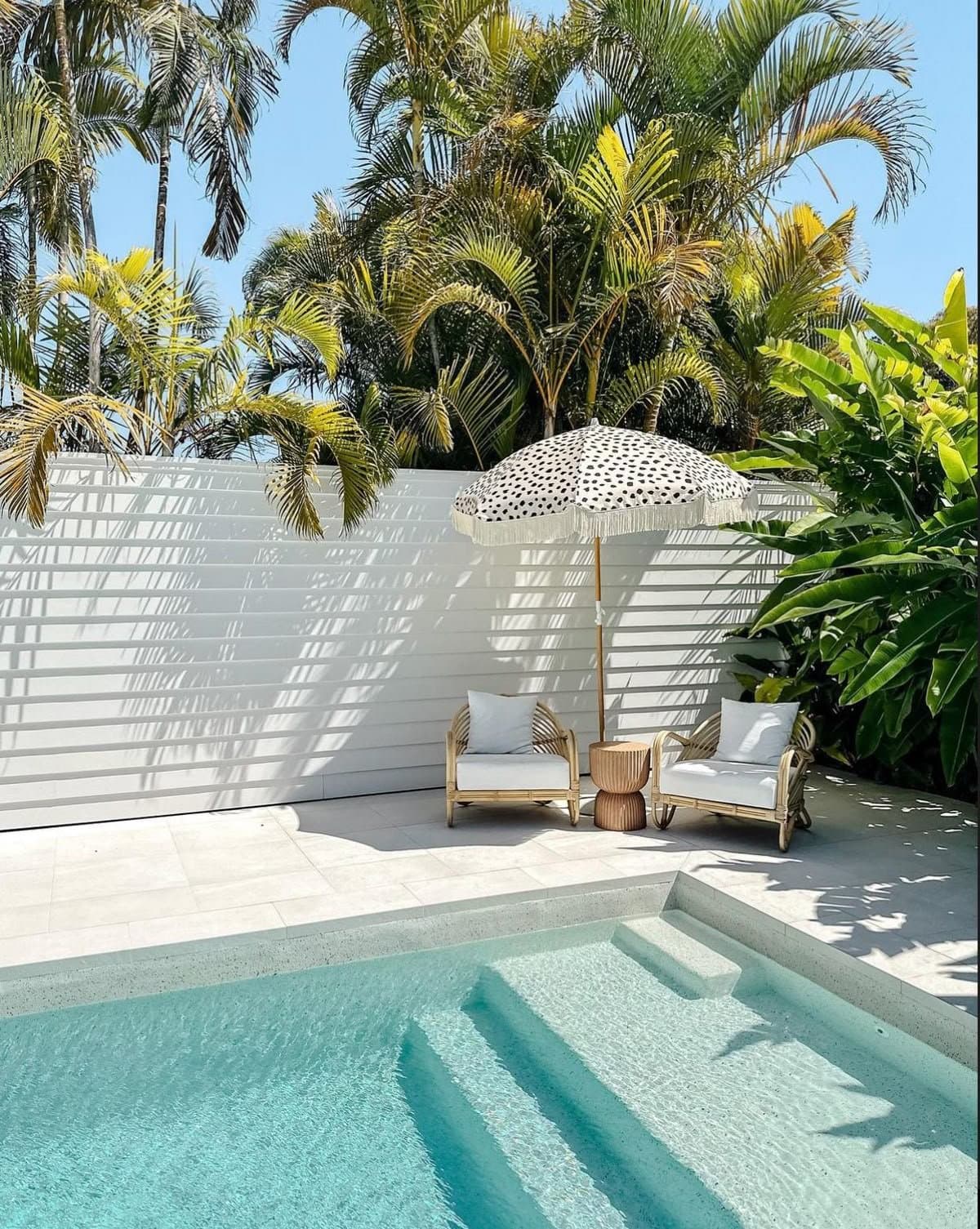 Piscina pequena com poltronas de vime e guarda-sol de bolinhas